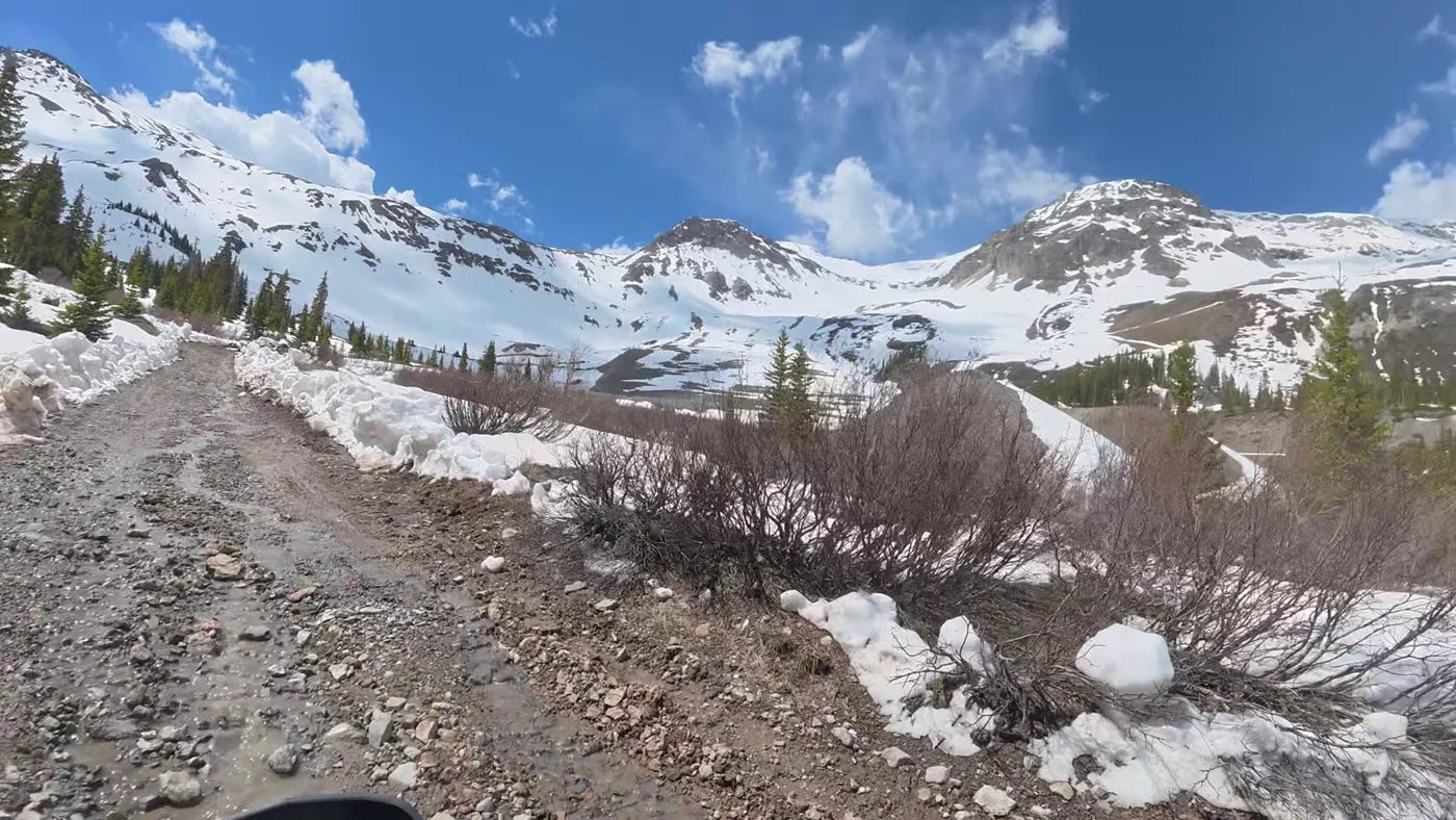 A rocky two-track climbing through late-spring snowbanks toward high peaks.
